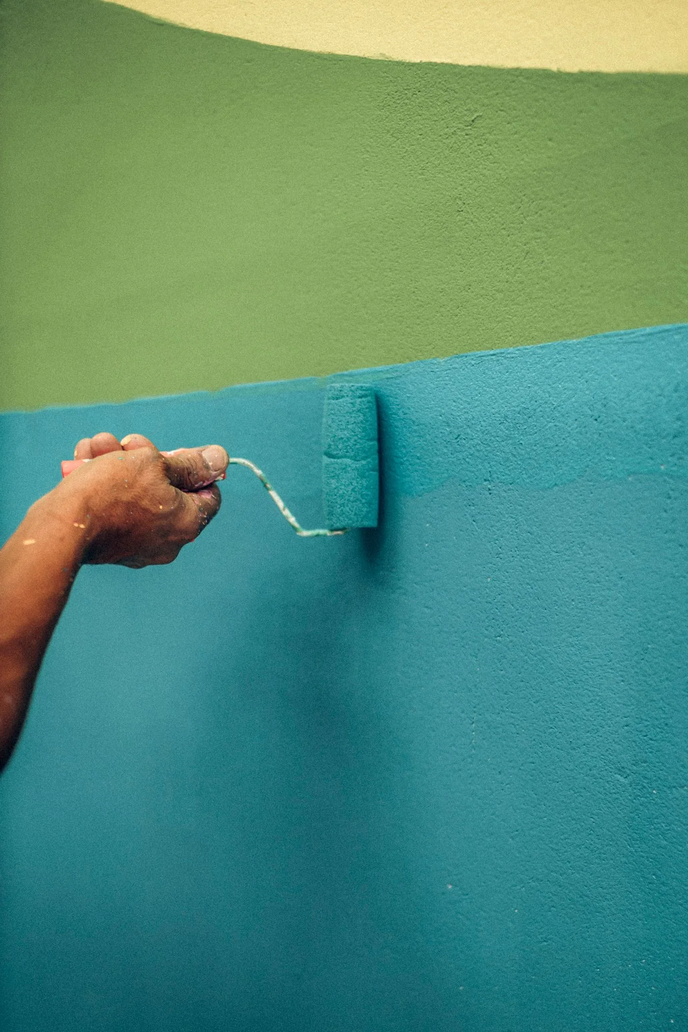 Une main passe un rouleau de peinture turquoise sur un mur