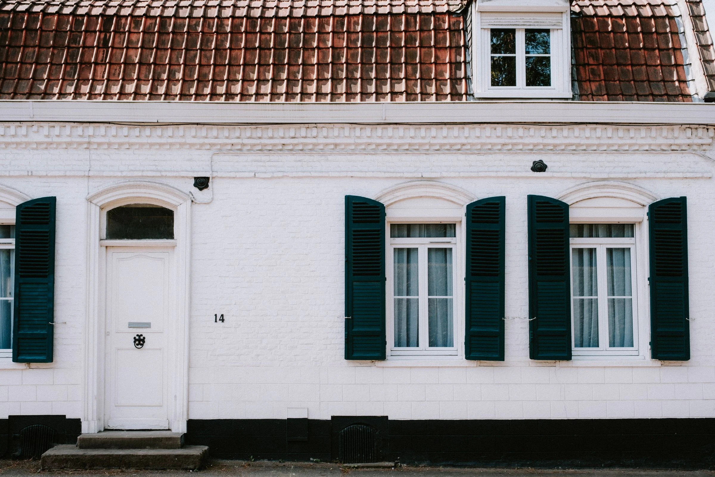 Une maison aux murs de brique peints en blanc, avec des volets vert foncé et une porte d'entrée blanche