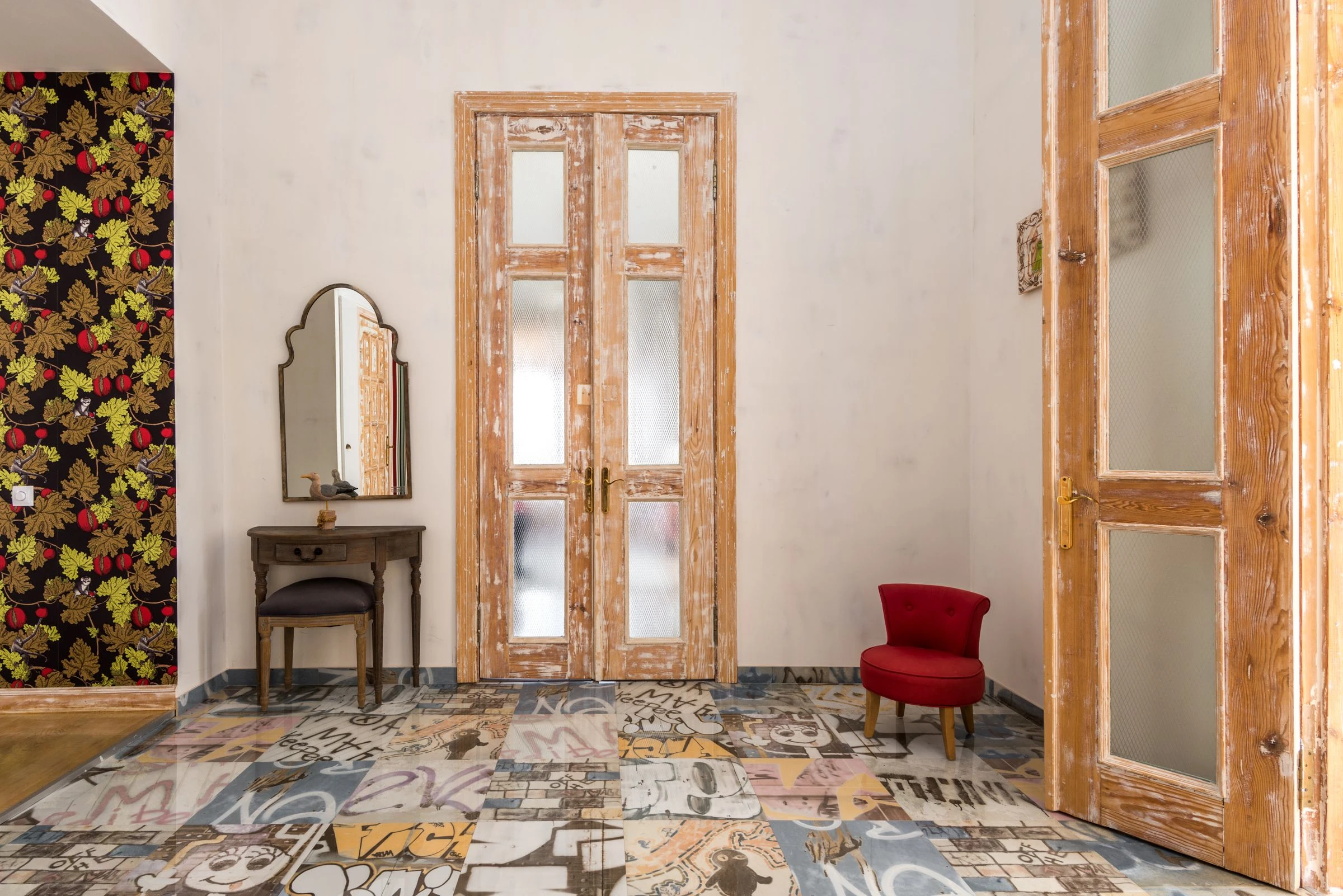 Une entrée aux portes anciennes en bois décapé, avec un pan de papier peint à fleurs et un sol de carreaux de ciment